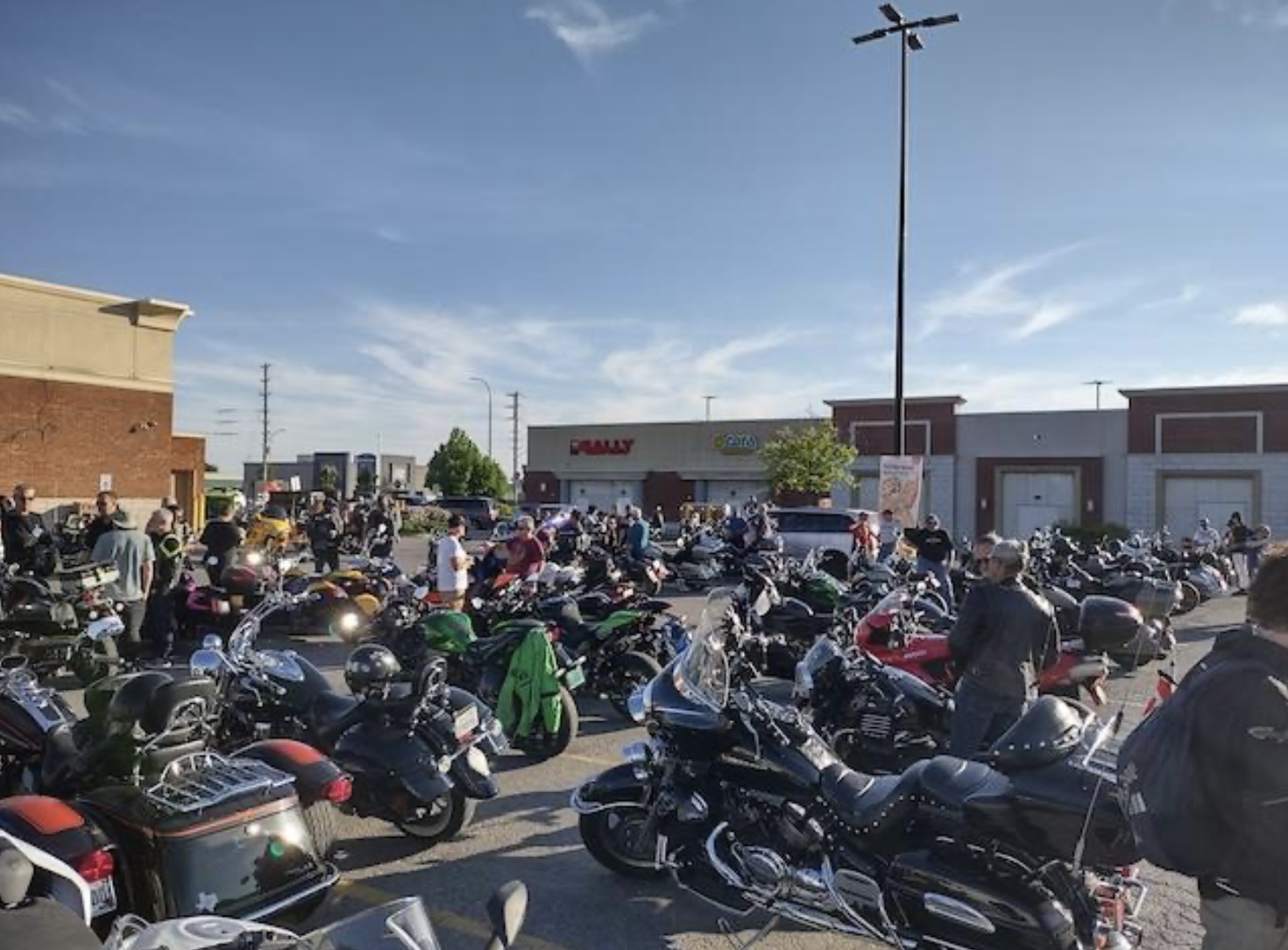 A strip mall parking lot on a summer afternoon filled with rows of parked motorcycles.