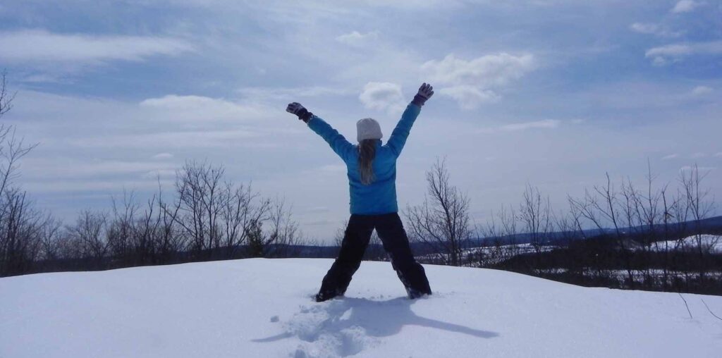 Une jeune fille se tient triomphante face aux paysages enneigés. Elle vient de grimper une colline, dans la neige.