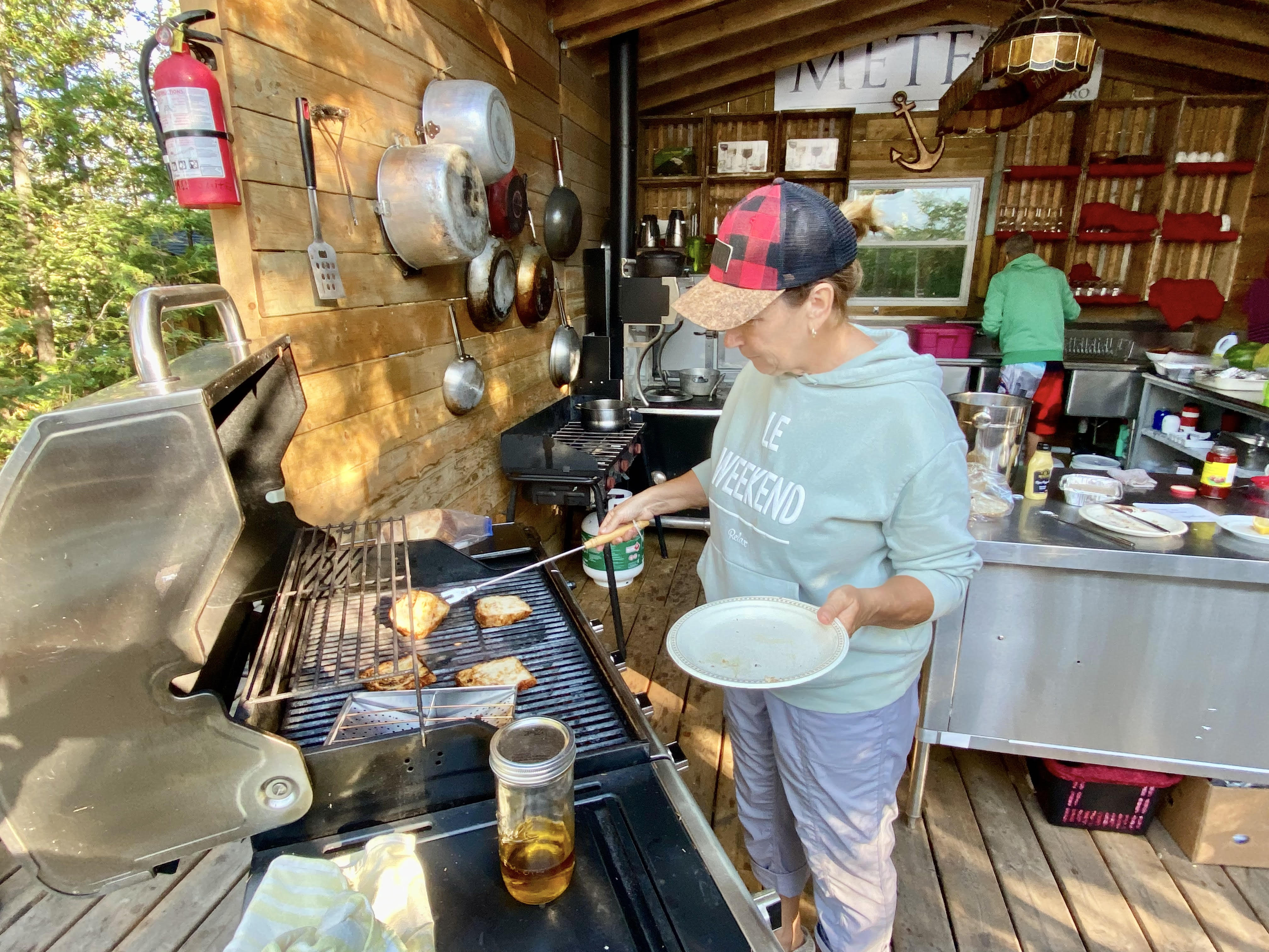 Une femme cuisine sur le BBQ, dans une cuisine extérieure avec toiture.