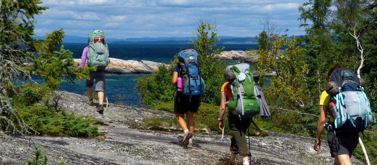 Un groupe de randonneurs marche en direction des rivers rocailleuses du lac Supérieur. Quelques arbres poussent entre les rochers.