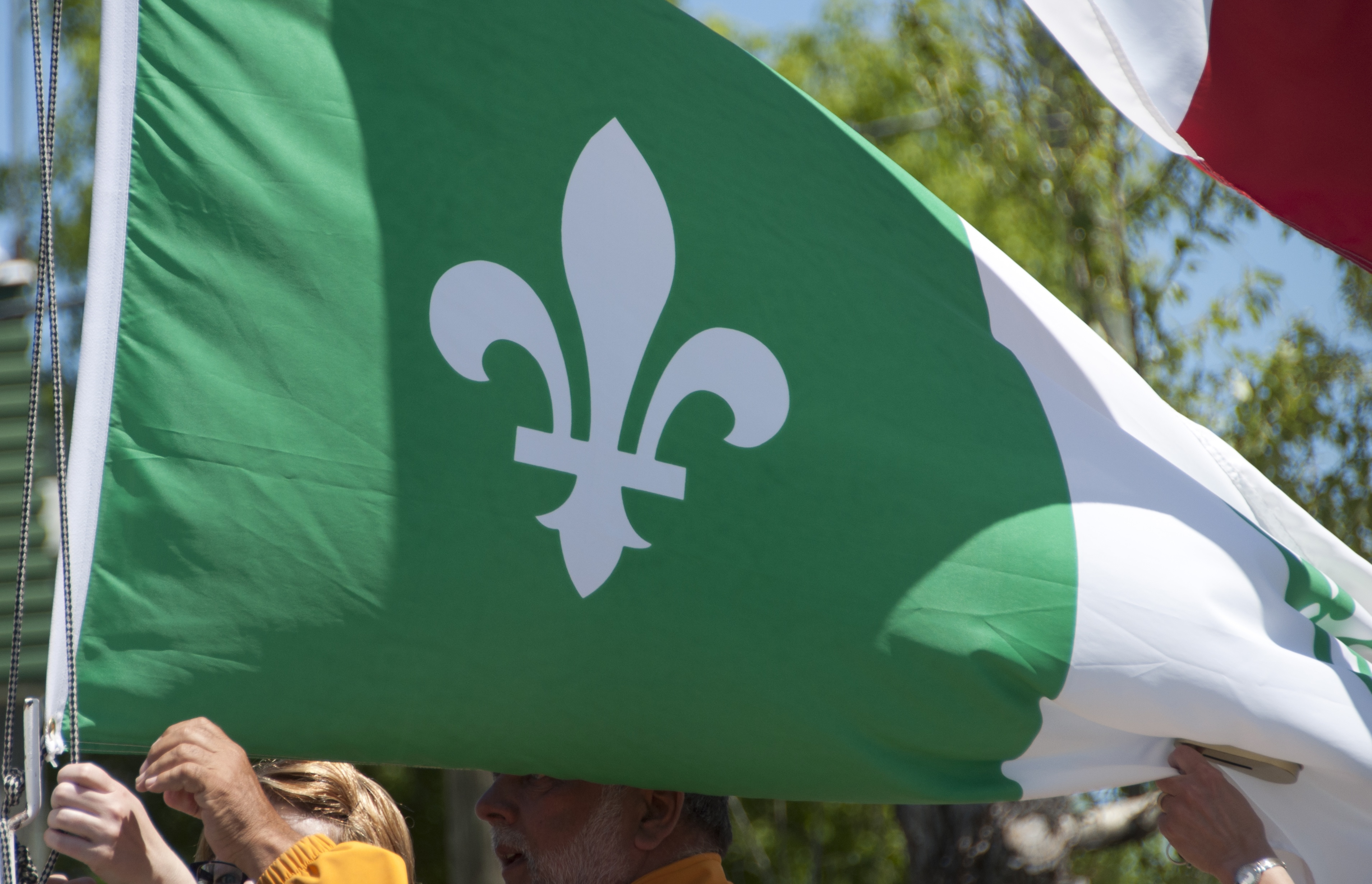 Un drapeau franco-ontarien flottant fièrement dans la brise alors qu'il est soulevé par plusieurs mains.