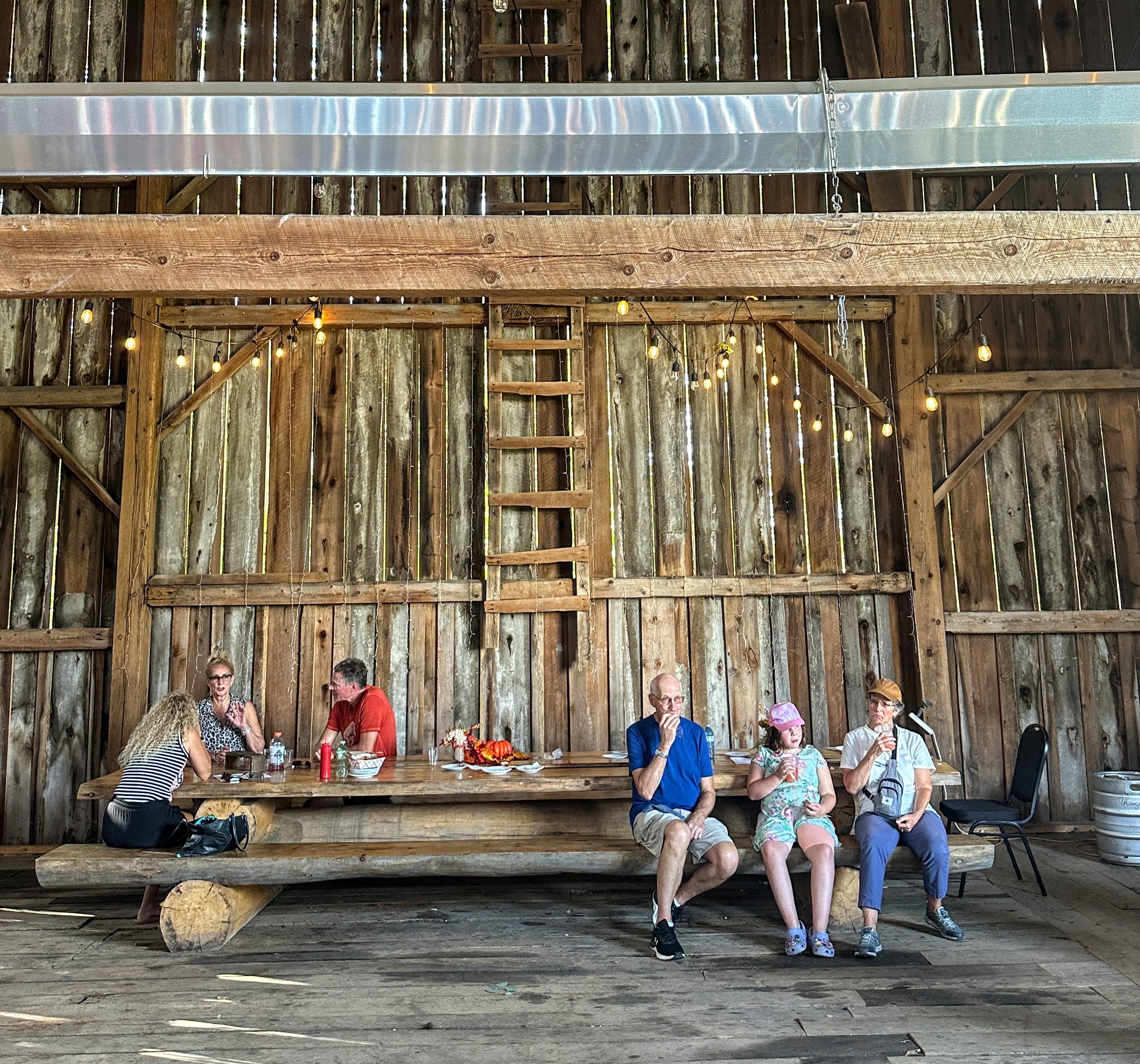 les visiteurs sirotent joyeusement du cidre à une table en bois à l'intérieur de la grange à vin rustique mais élégante en bois de Thompson Farms.