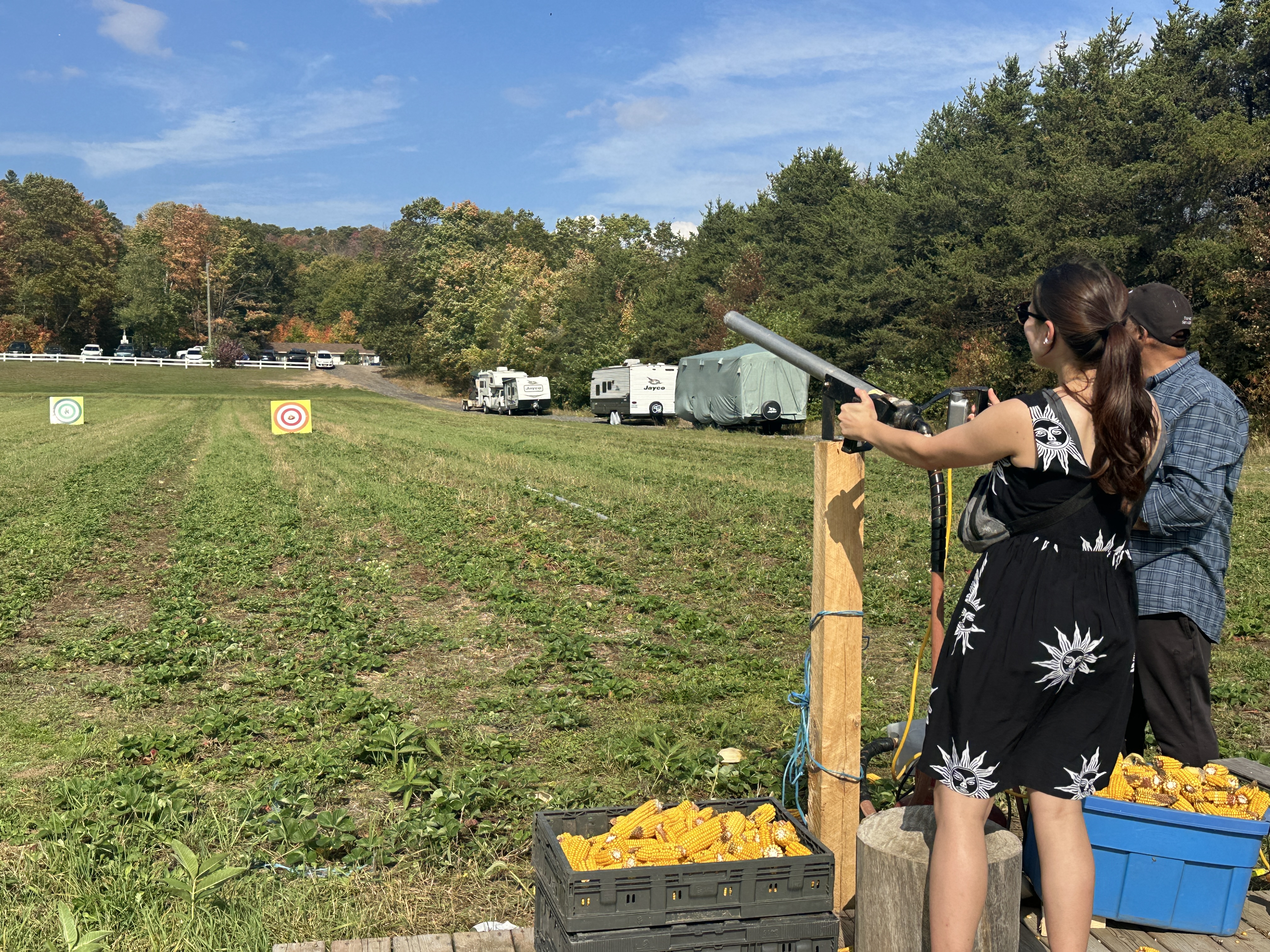 une femme rieuse tire un canon à épis de maïs sur des cibles dans un champ vert au festival d'automne de Thompson Farms.