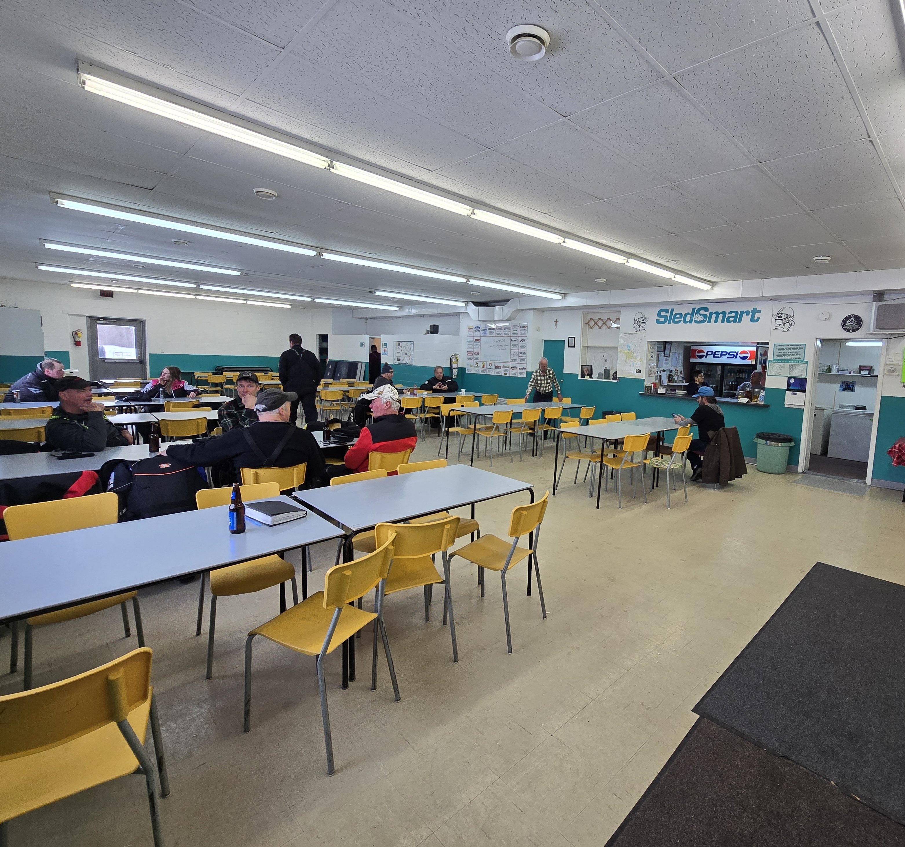 Les gens sont assis à de longues tables dans une grande salle de réunion du club-house du Club de As à Moonbeam, en Ontario.