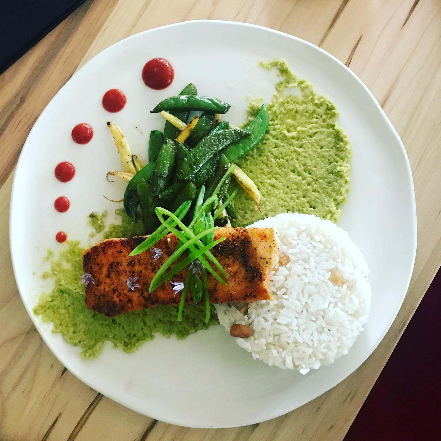 an artistically plated dish with salmon and rice arranged with colourful dots of sauces and carefully laid julienned vegetables.