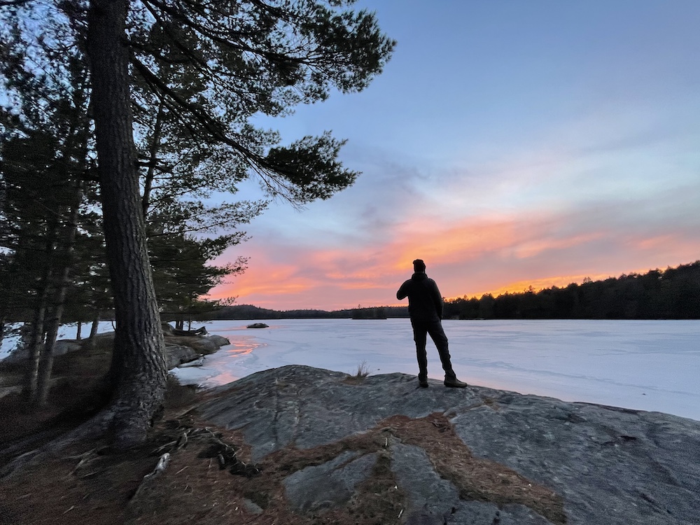 Man standing on rocky shore looking out across frozen lake