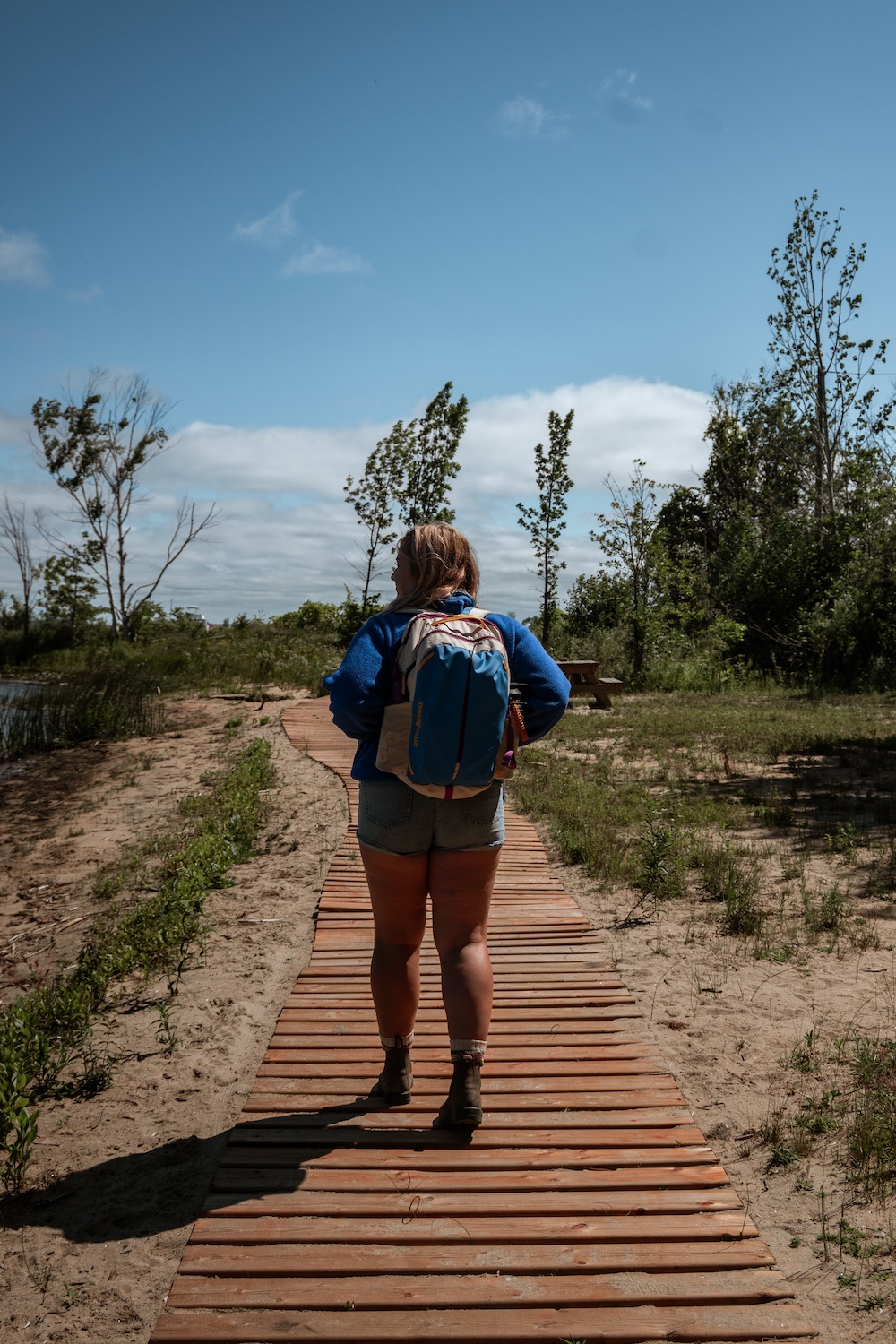 Woman wearing backpack walking on a boardwalk over sand