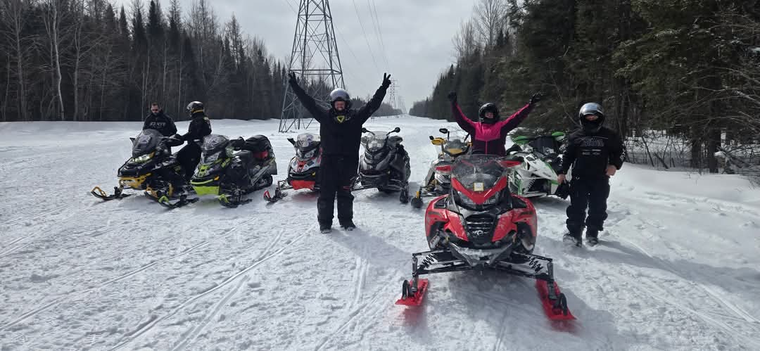 Des motoneigistes sont regroupés sur un sentier de motoneige qui suit une ligne d'hydroélectricité