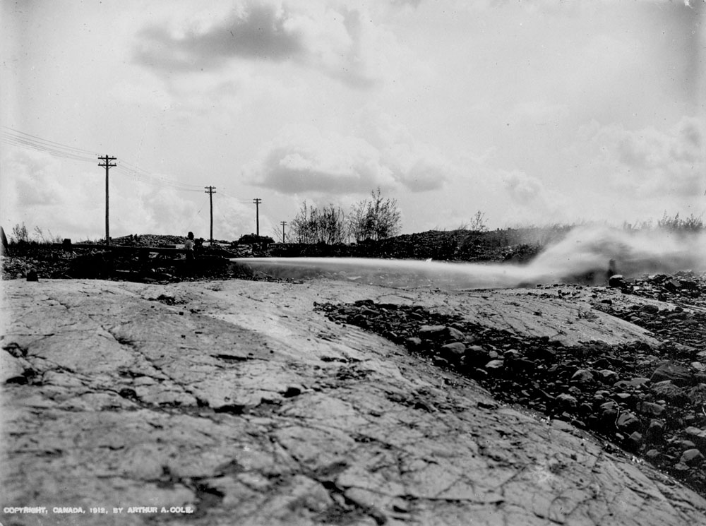 Des rochers sont dénués. Au loin, on voit de la fumée s'échapper des crevasses.