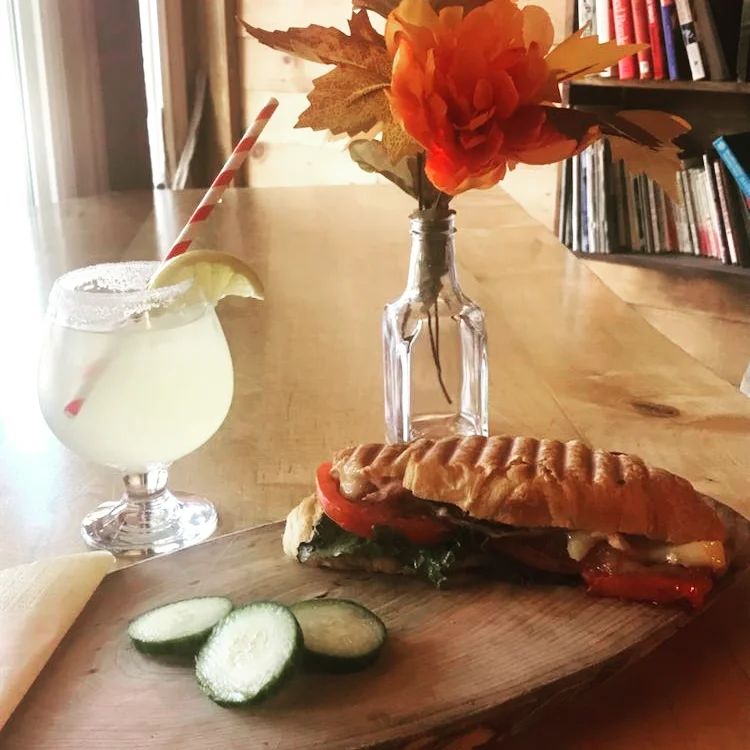 Un délicieux sandwich de charcuterie sur du pain français, accompagné d'un cocktail au citron et d'un vase de fleurs.