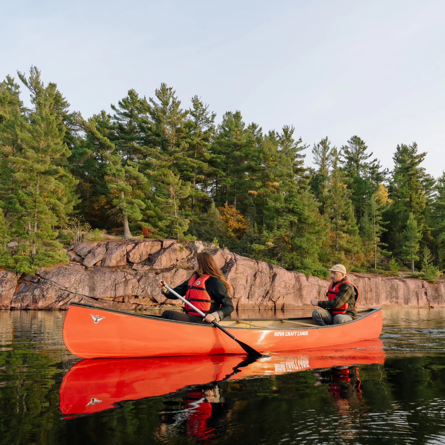 Deux personnes pagayent en canoë sur une eau lisse comme un miroir, au milieu des rives boisées du territoire non cédé de Wikwemikong.
