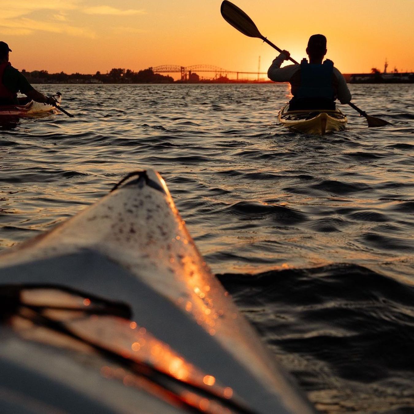 Des kayakistes pagayent sur la rivière Sainte Marys en direction de Sault-Sainte-Marie, l'eau illuminée par un coucher de soleil doré.