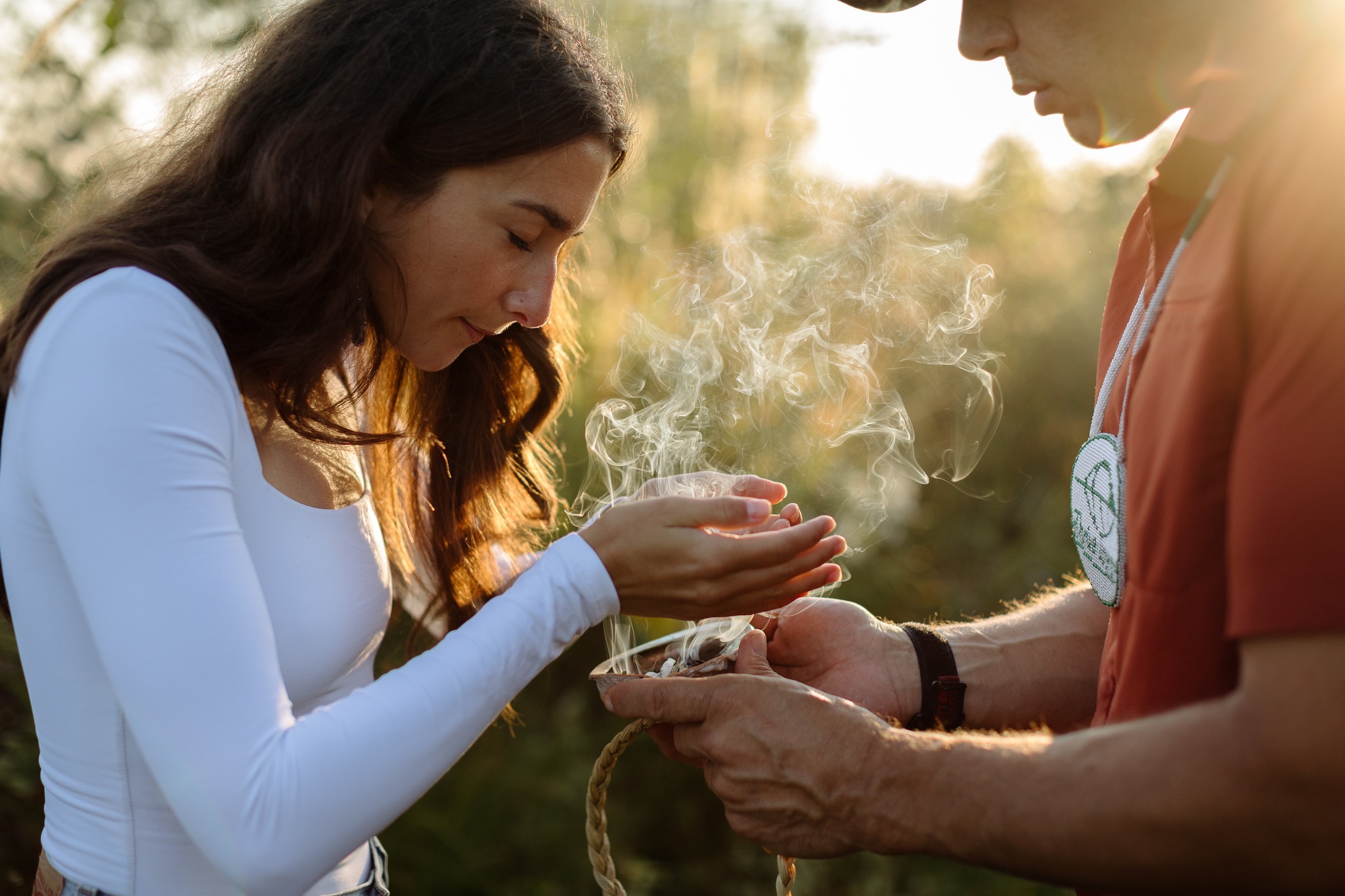 Un guide de Thrive Tours tient un bol utilisé pour le smudging pour une femme qui recueille la fumée dans ses mains.