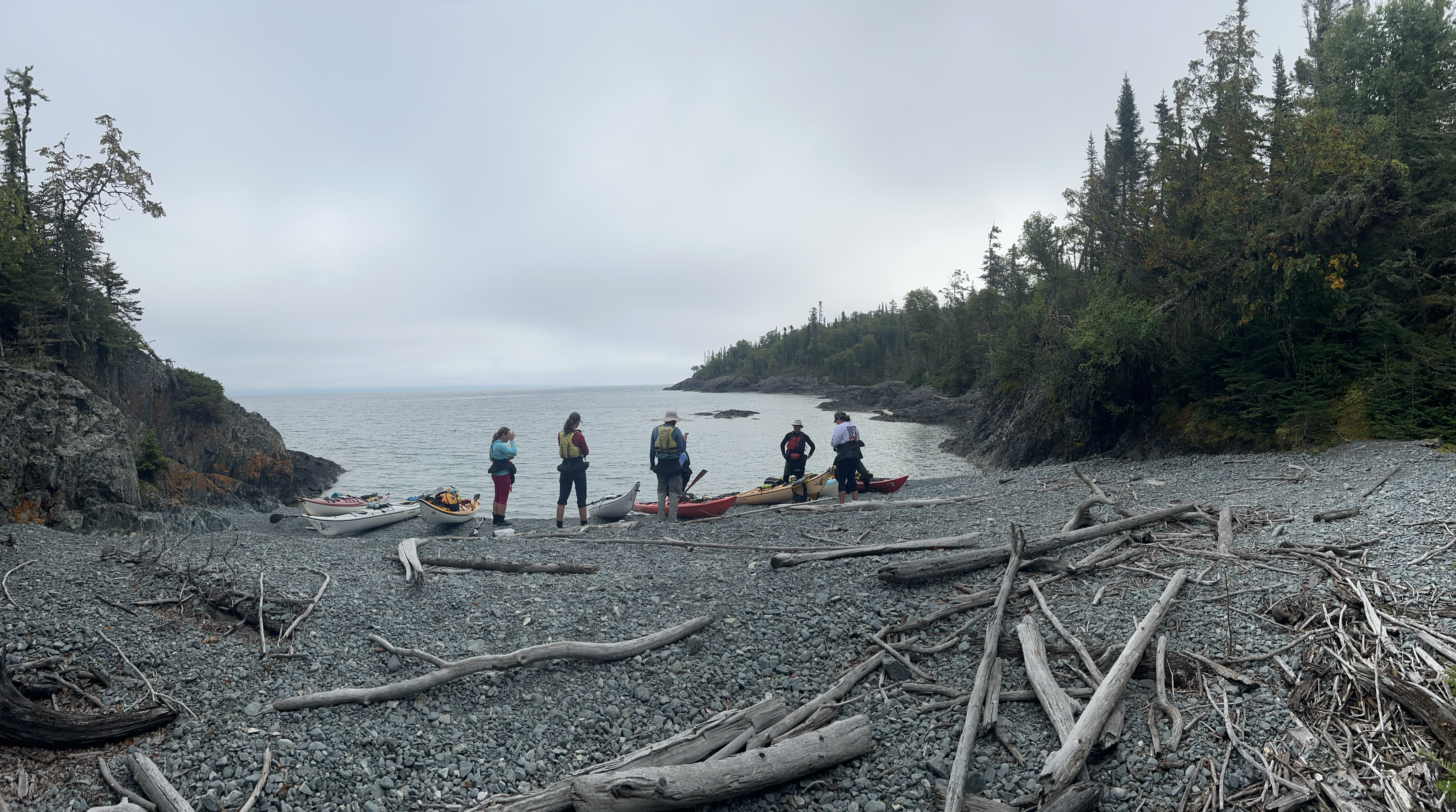 Une rangée de pagayeurs se tient sur une plage de gravier avec leurs kayaks sur l'île Mortimer, dans le lac Supérieur.