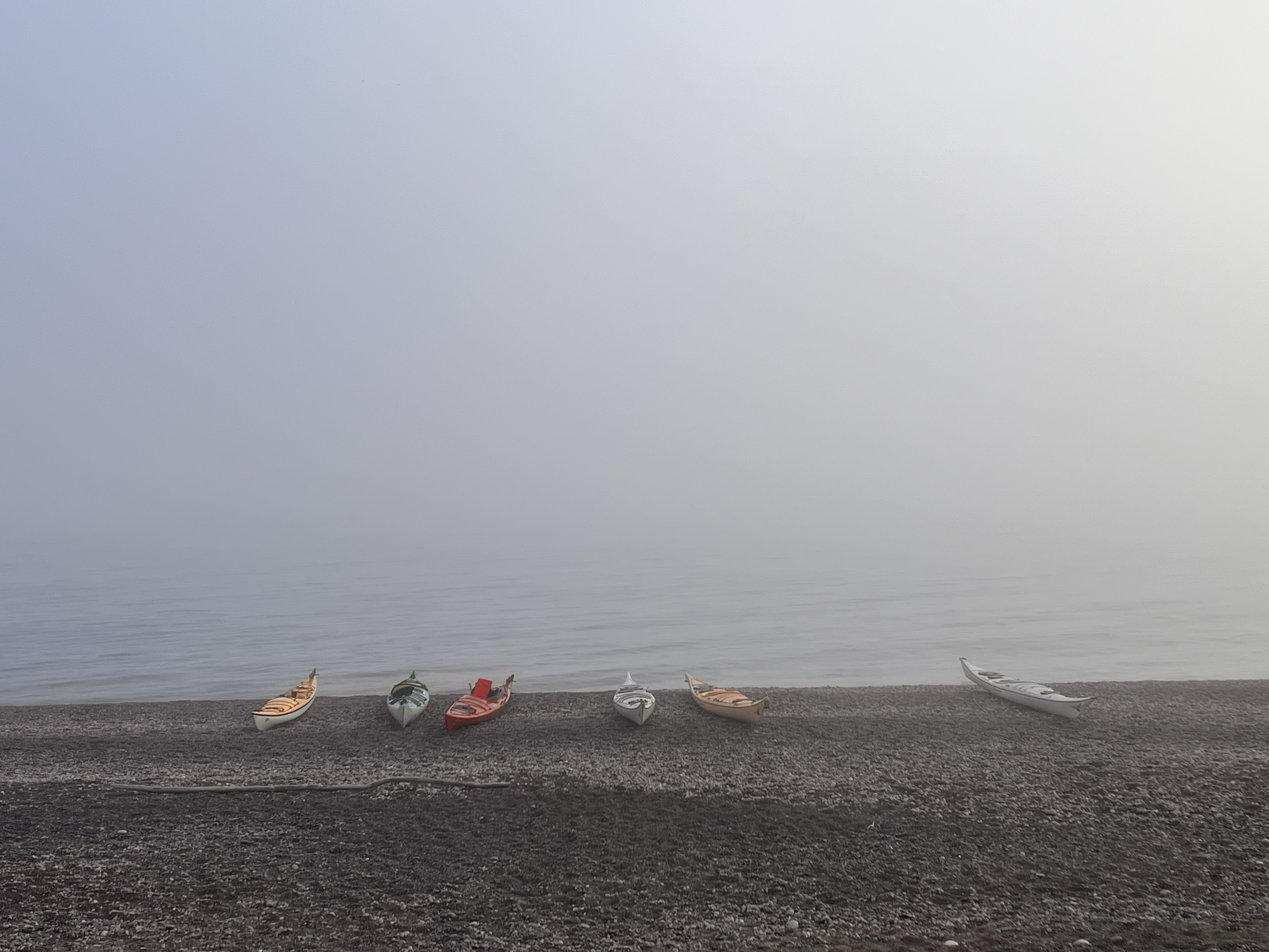 Une rangée de kayaks sur une plage de sable, devant un mur de brume matinale grise recouvrant l'immensité du lac Supérieur.