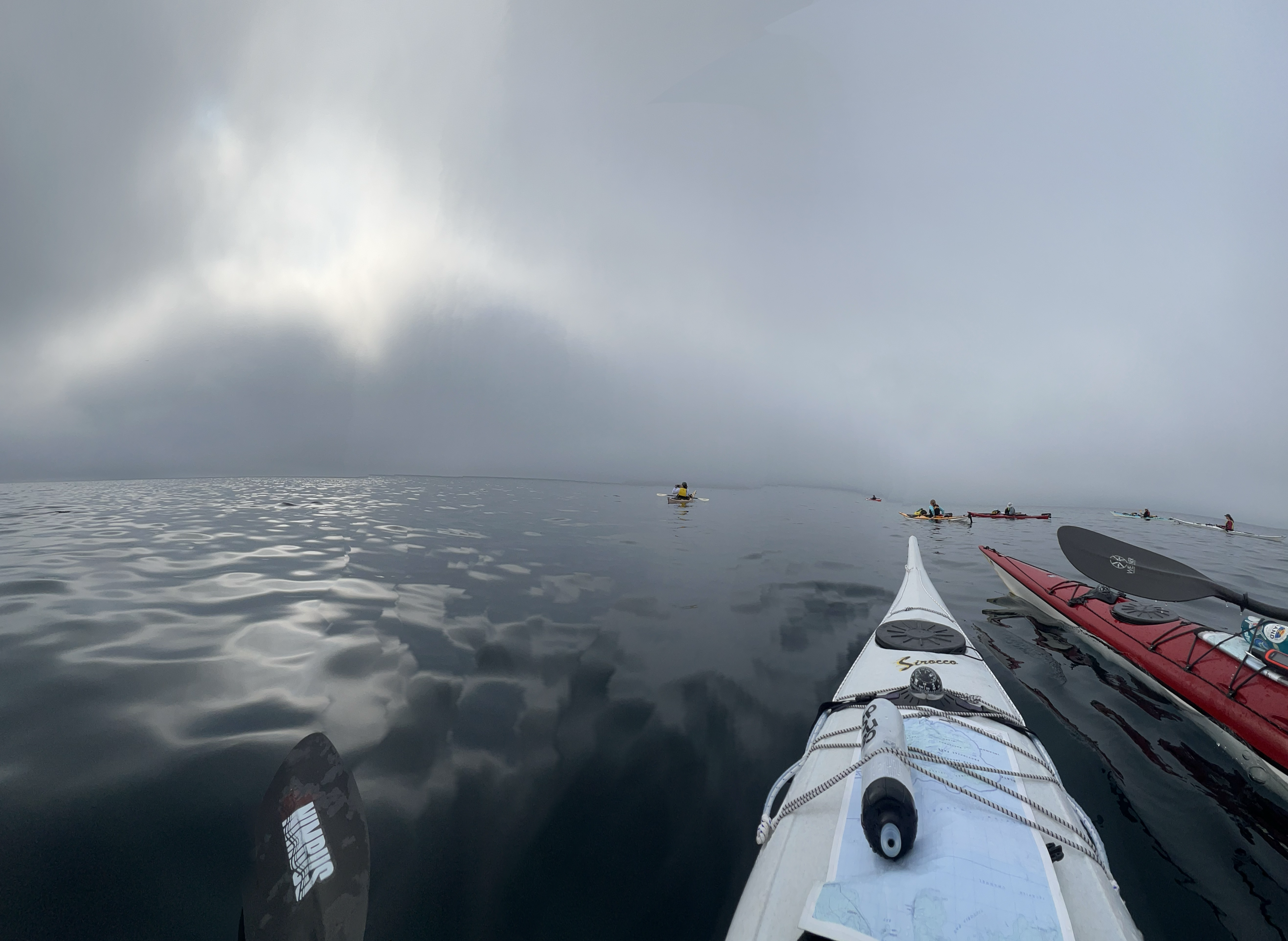 Des kayaks glissent sur les eaux sombres et lisses du lac Supérieur, sous d'épais nuages ​​gris et à perte de vue, l'horizon s'étendant à l'infini sur une étendue d'eau libre.