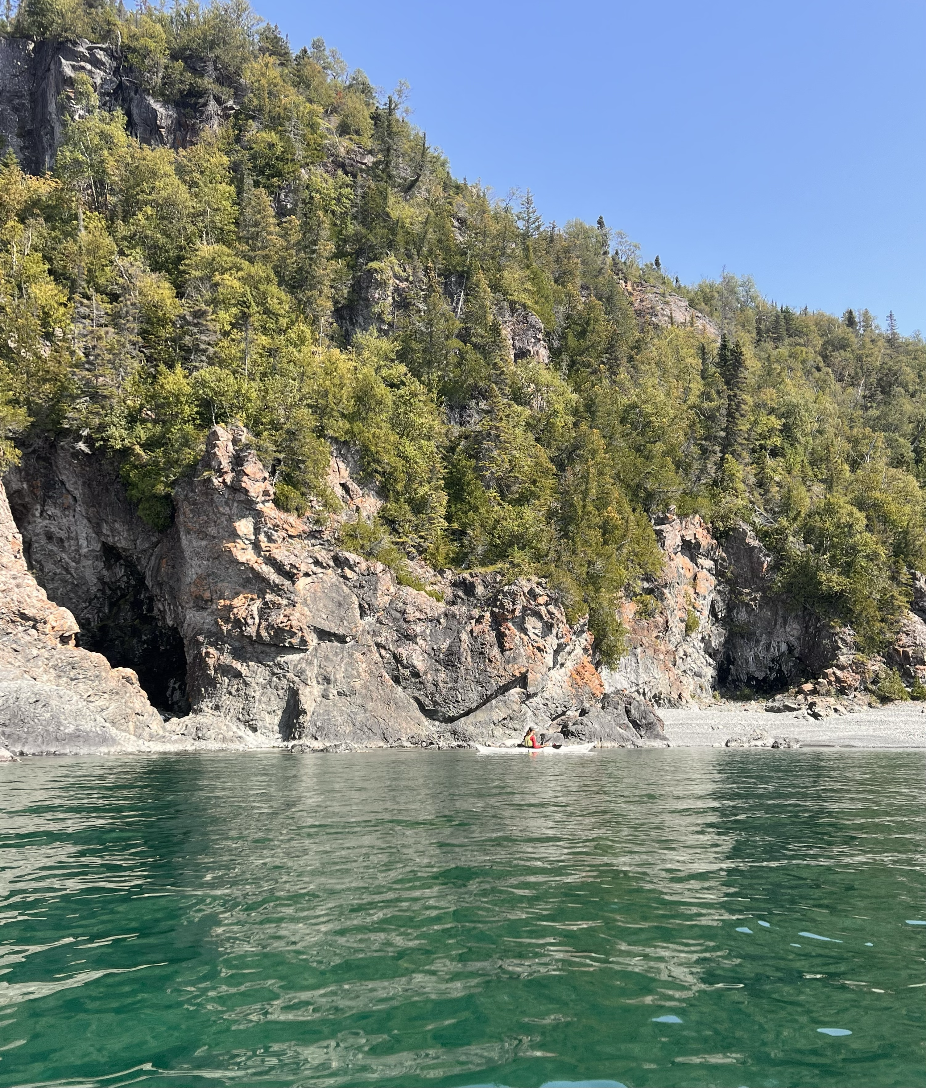 Les eaux turquoise du lac Supérieur rencontrent une plage de sable blanc et une falaise abrupte surmontée d'une épaisse forêt verdoyante sous un ciel d'un bleu limpide.