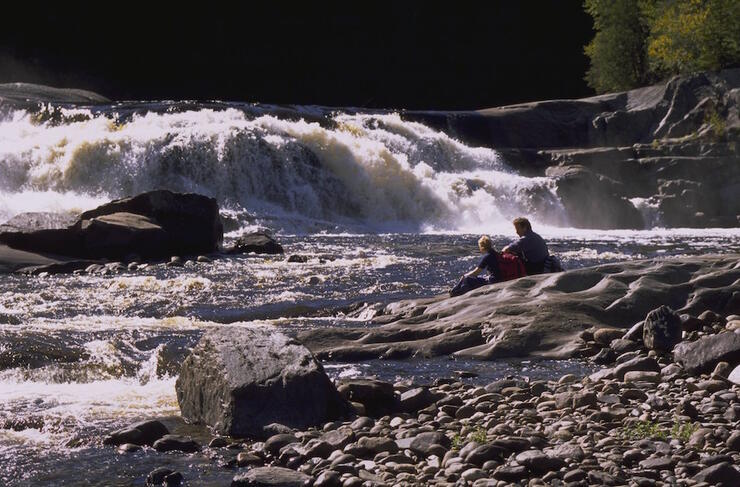 Two people sitting on a rock looking a a small waterfall