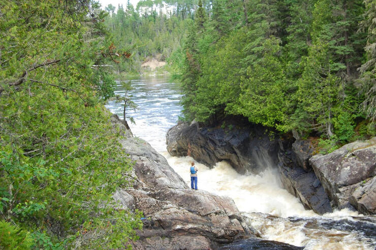 Person standing beside a cascading waterfall. 