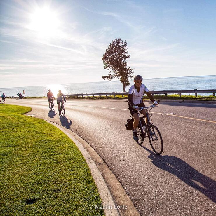 Cyclists pedalling on a highway along a lake.