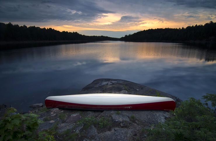 Canoe resting on shore of lake at sunset