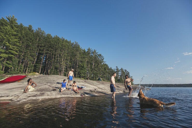 Group of family and friends relaxing on a rocky shoreline and playing in the lake.