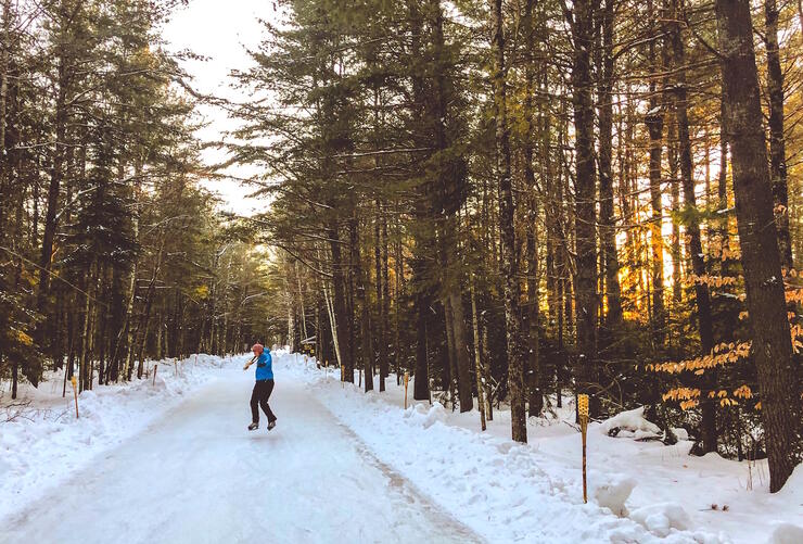 Woman skating on ice trail surrounded by tall trees 