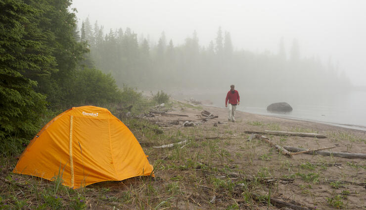 Yellow tent set up on beach near lake backcountry camping on crown land in Ontario.